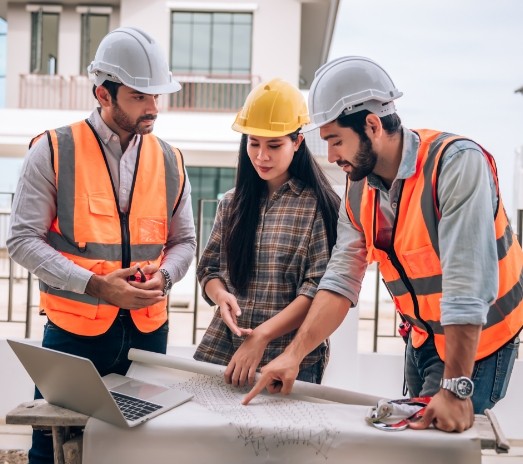 Grupo de ingenieros y arquitecta revisando planos de construcción en una obra, usando cascos y chalecos de seguridad