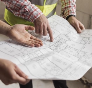 Manos de profesionales señalando un plano arquitectónico durante una revisión en obra